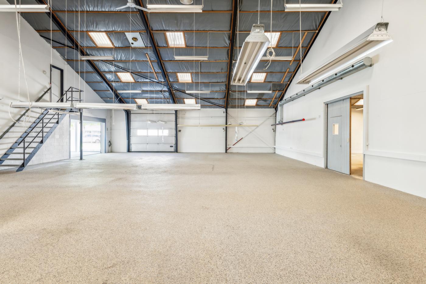 A high, pitched workshop hall at Landbrugsvej 6 with an epoxy floor and an overhead door